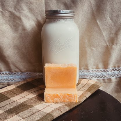 non-colored bars of goat milk soap in front of jar of fresh goat milk.